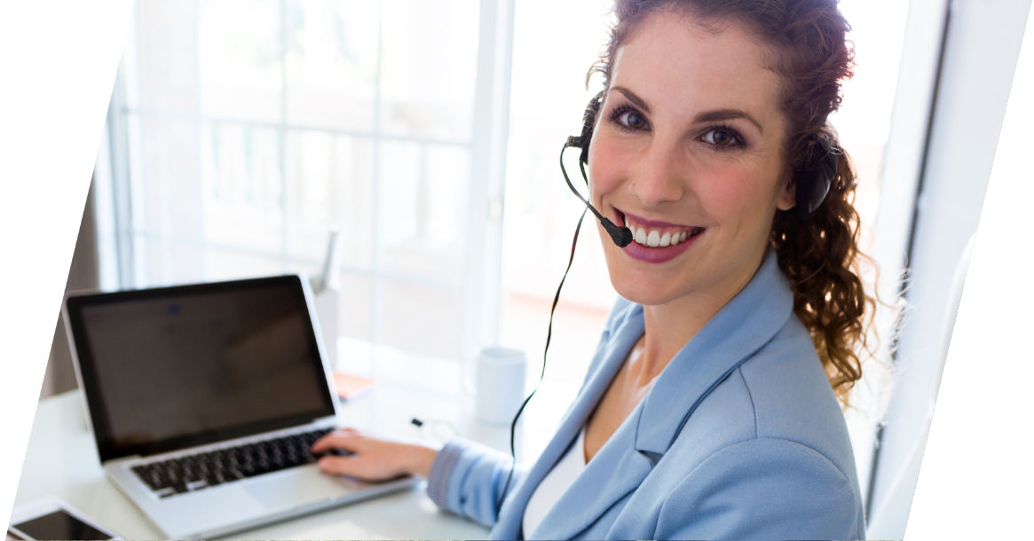Junge Frau mit brünettem gewellten Haar sitzt vor Notebook und telefoniert über Headset